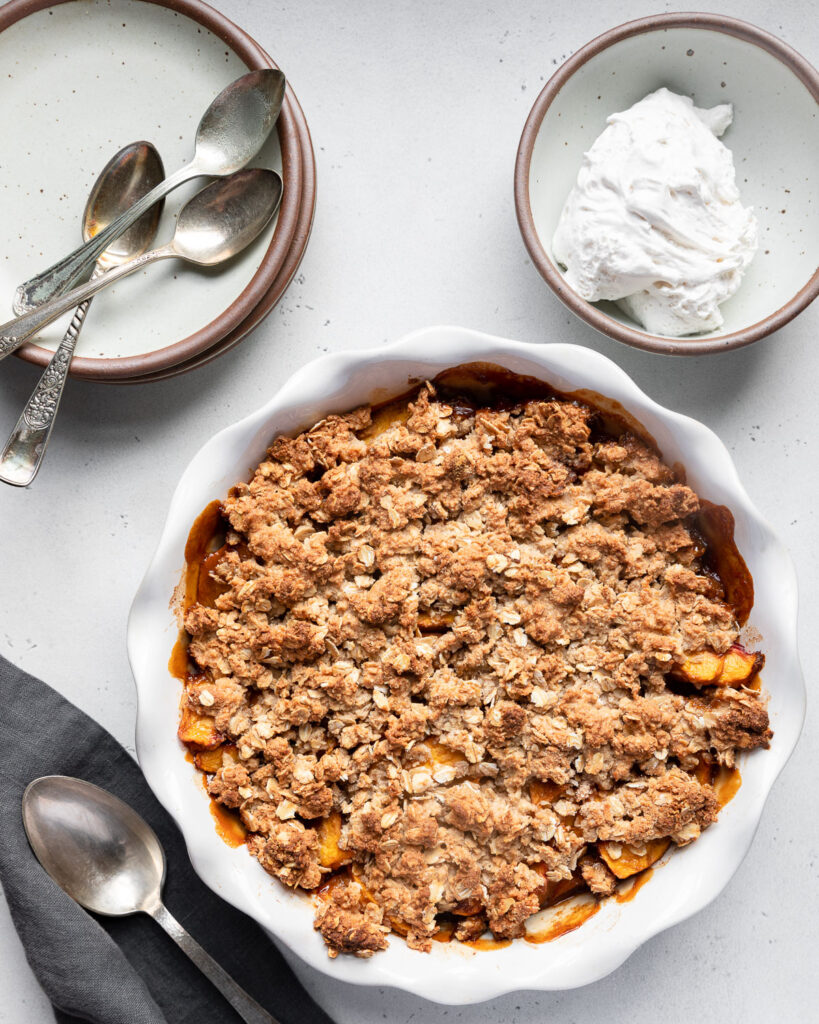 Healthier peach crisp, uncut crisp with whipped topping on side
