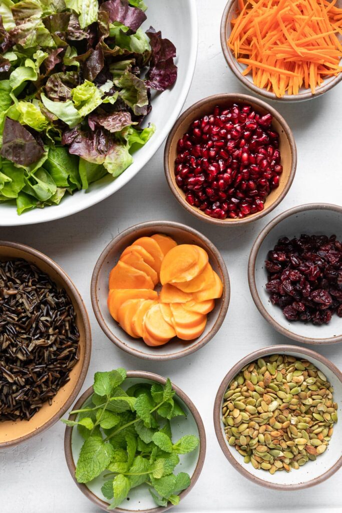 Wild Rice Holiday Salad ingredients: lettuce, carrots, pomegranate, persimmon, dried cranberries, wild rice, pumpkin seeds, mint